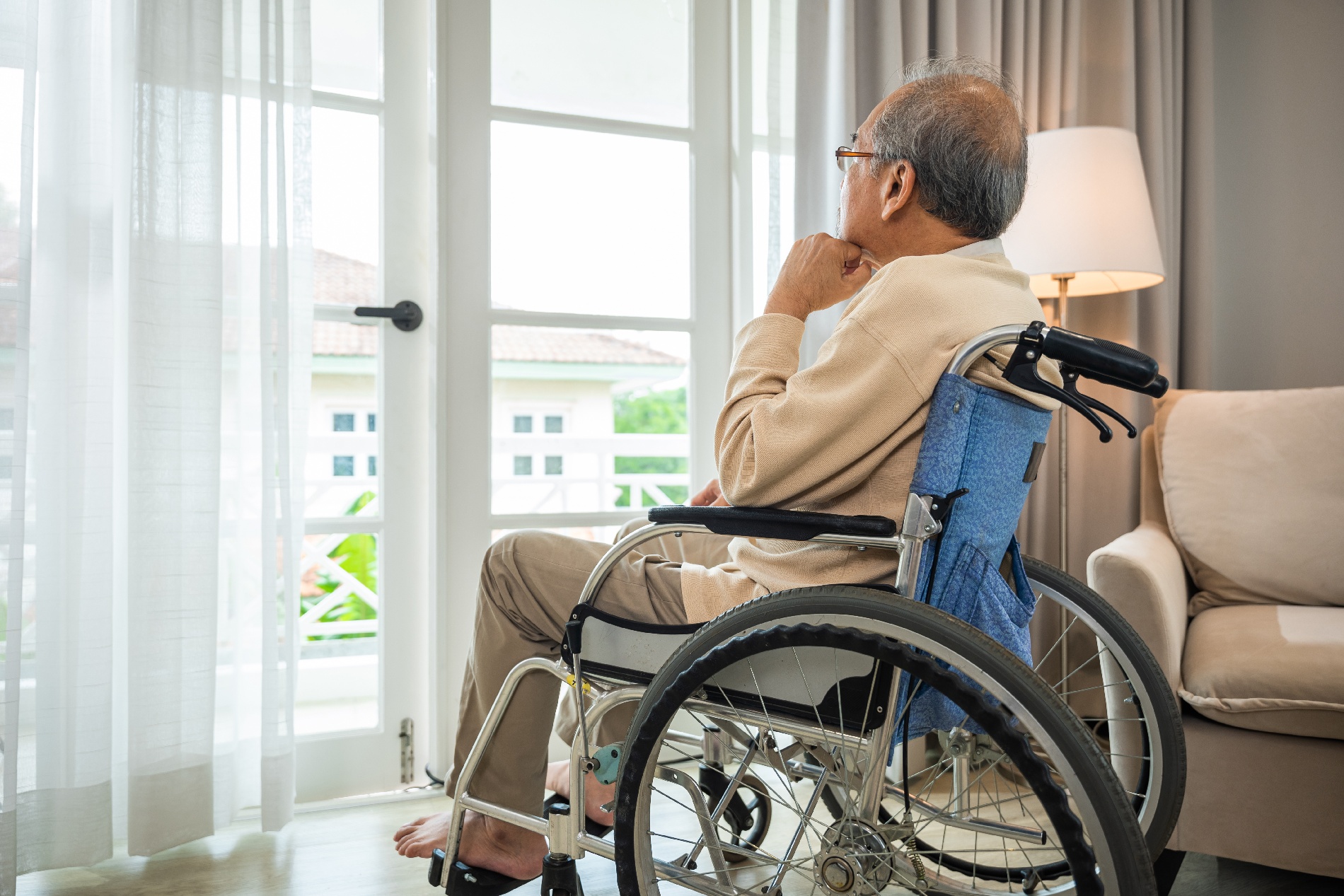A lonely man in a wheelchair stares out an open window of a high-rise condo.
