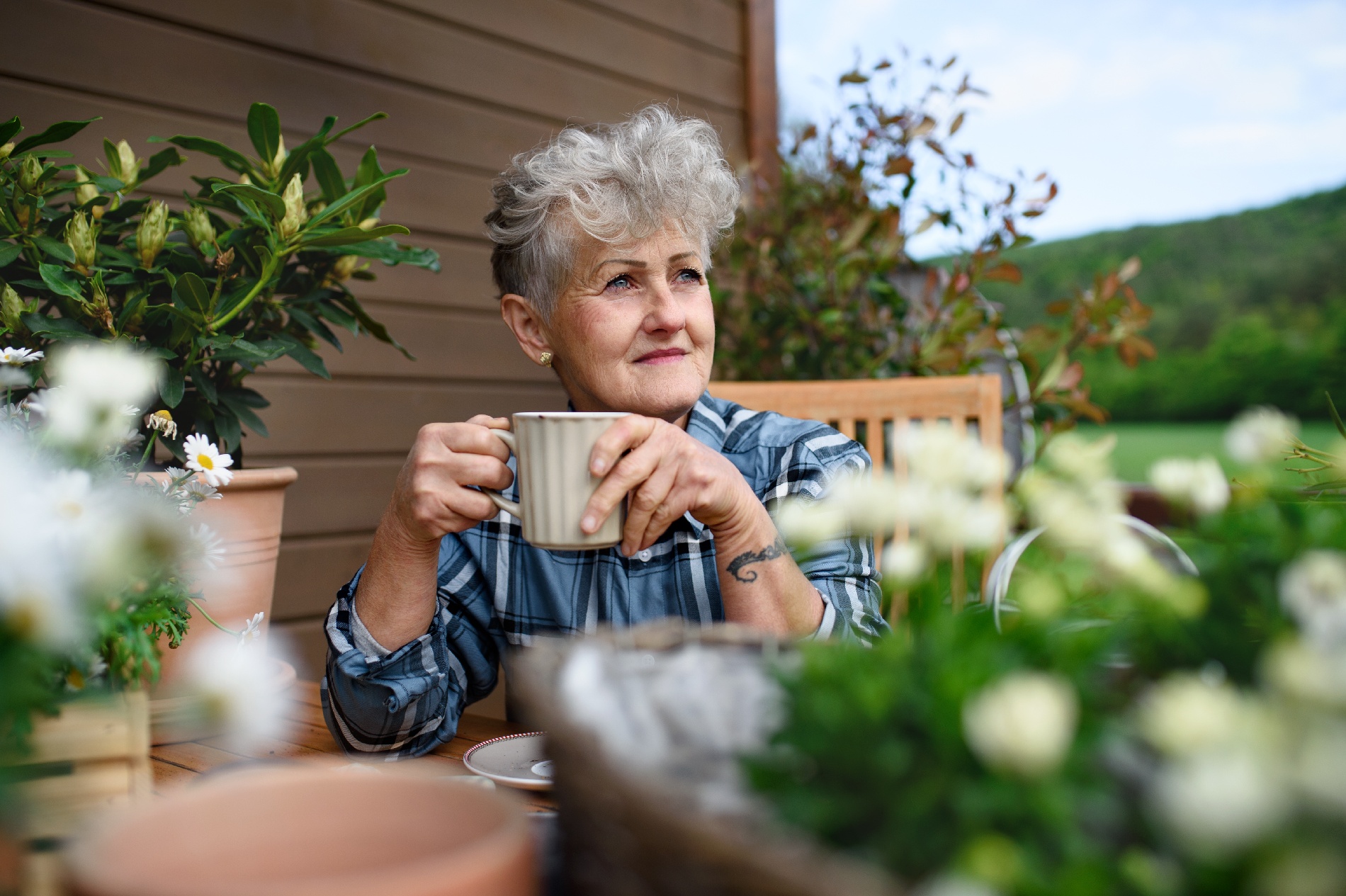 An older woman sits outside while drinking a cup of coffee alone. 