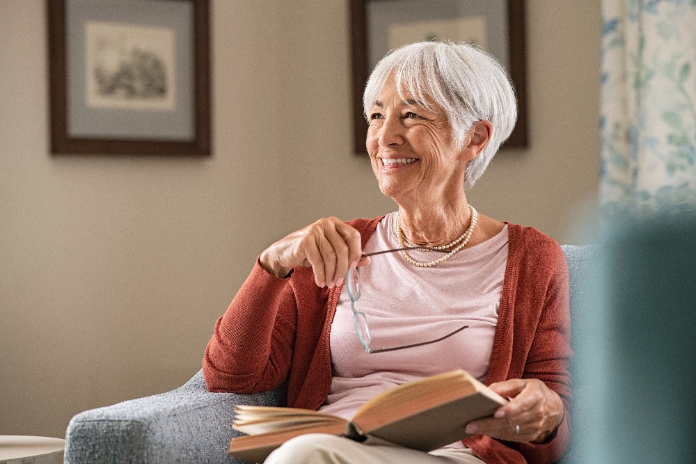 An smiling elderly woman takes a break from reading a book.