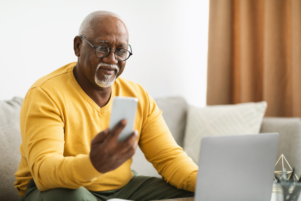 Mature businessman using cellphone and laptop on sofa.