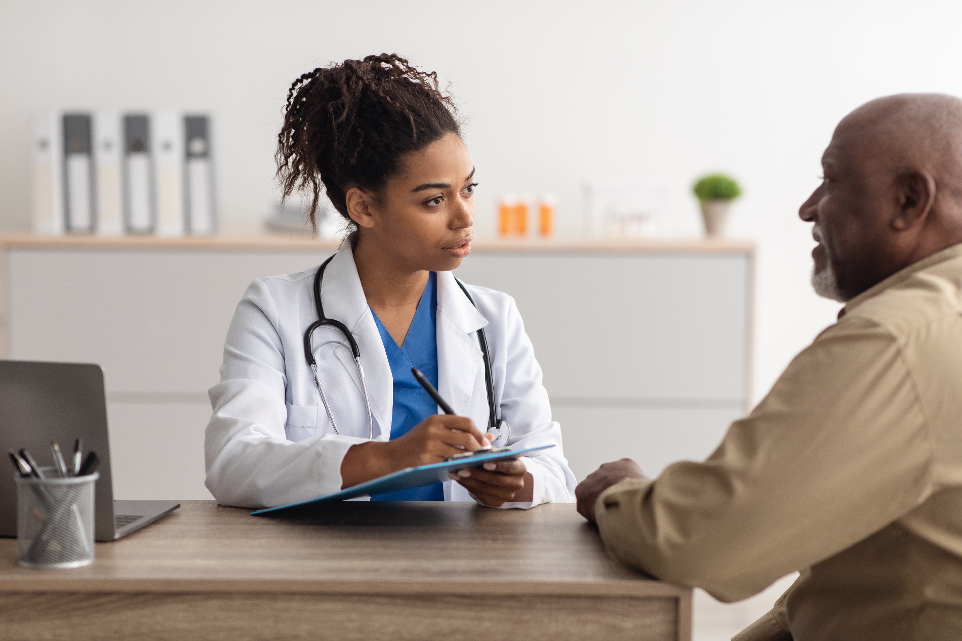 A doctor writing down notes as she talks to an older male patient.