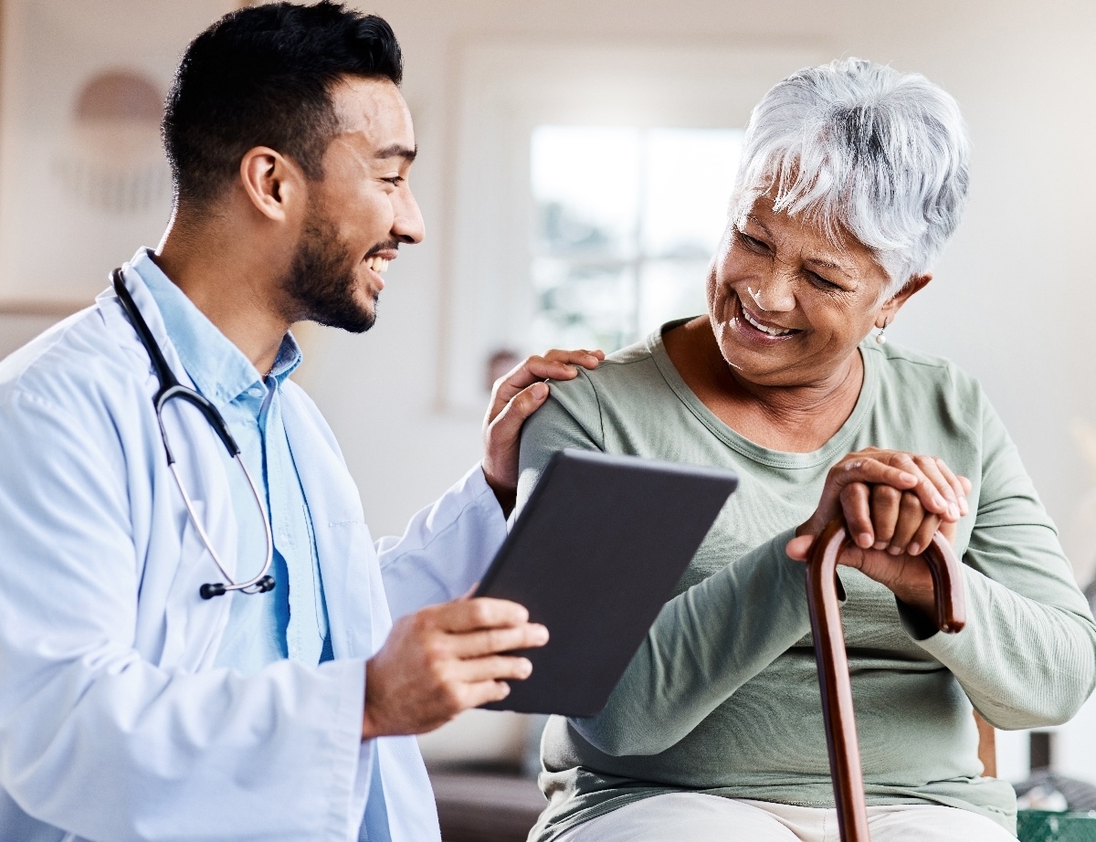 A male doctor talks to an older female patient while holding a chart.