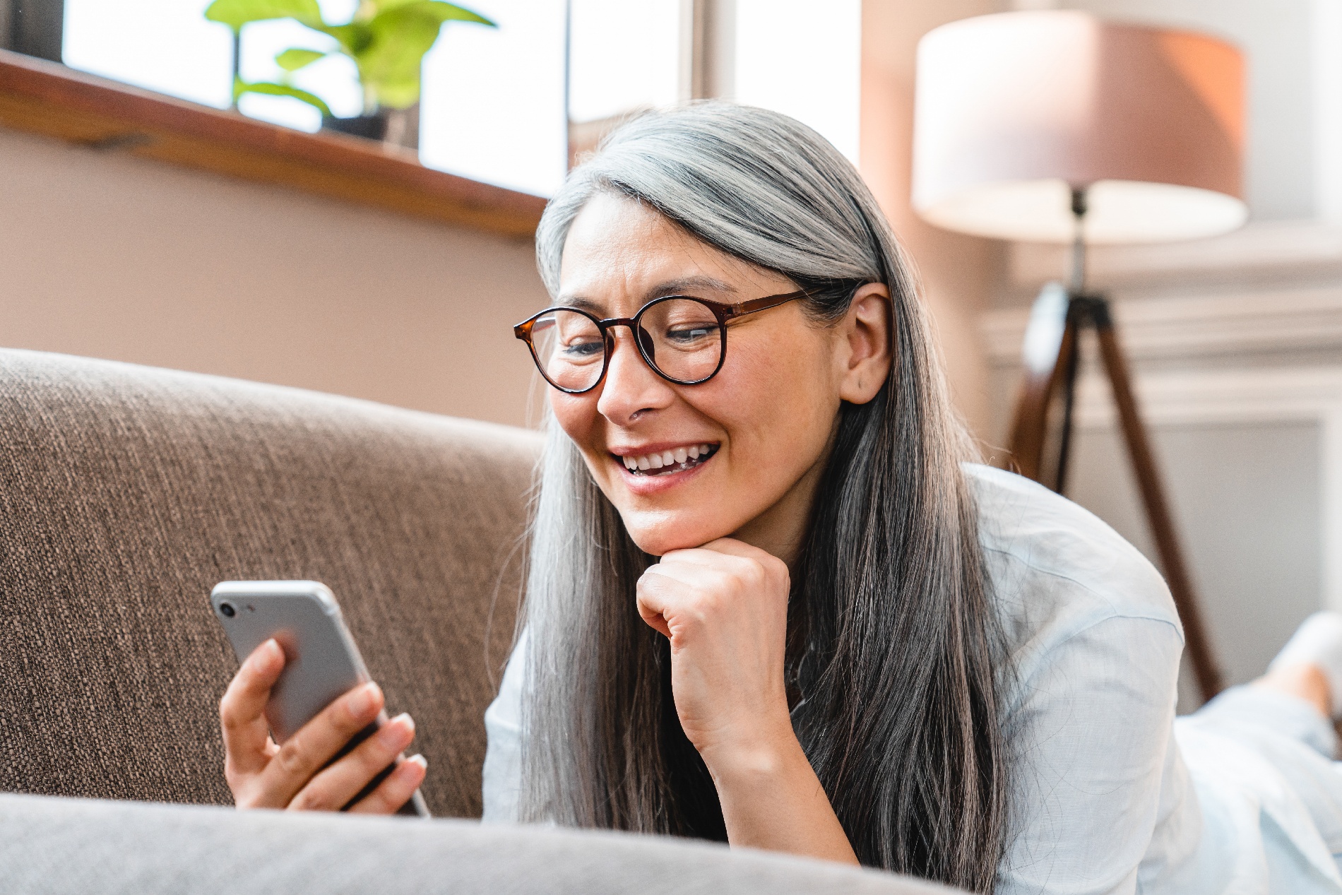 An older woman lying on a sofa and using the Pyx Health app on her cellphone. 