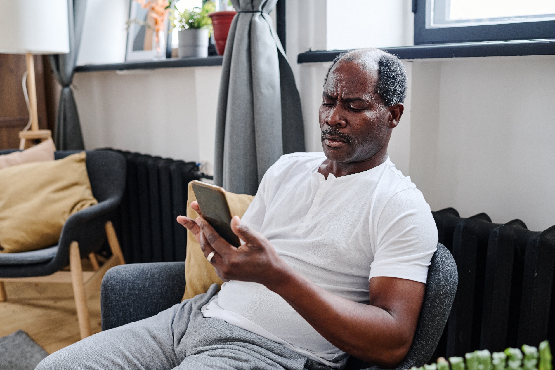 A middle-aged man sits in a chair in a doctor’s office while checking his cellphone. 