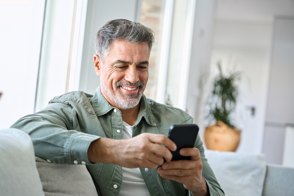 A man with grey hair and a beard using a cellphone to text.