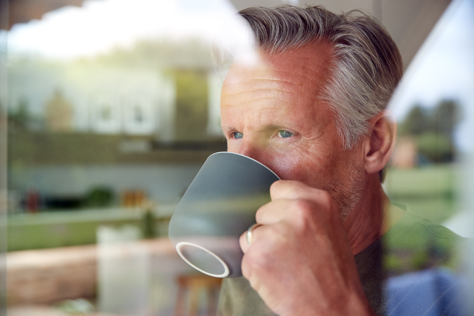 An older man sits alone drinking coffee as he stares out a window. 