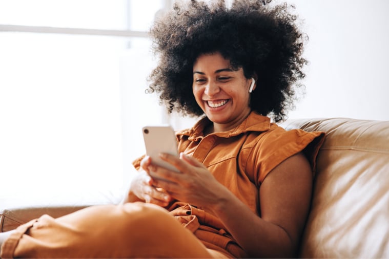 A woman having a video call on a smartphone while sitting on a sofa. 