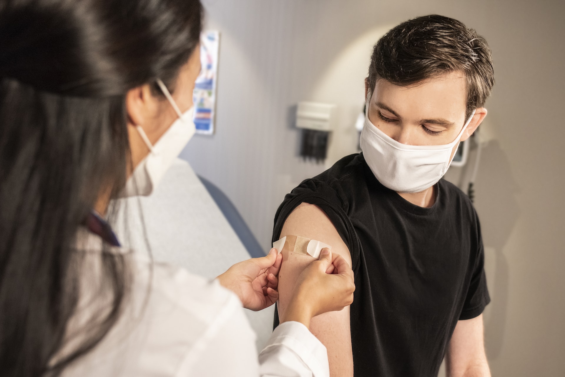 a female doctor applies a bandaid to a male patient's arm after receiving a vaccine