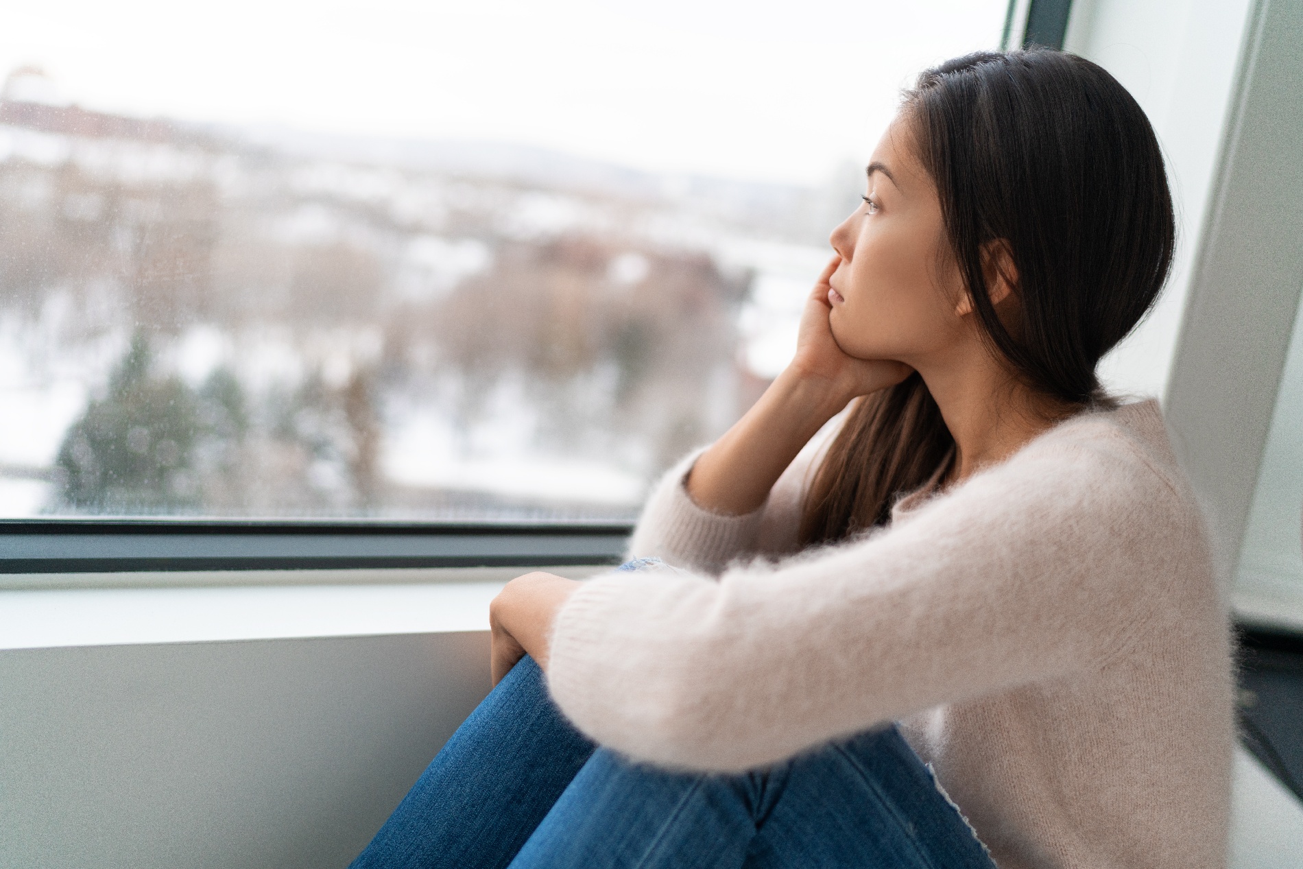A lonely young woman stares out a window in an empty room. 